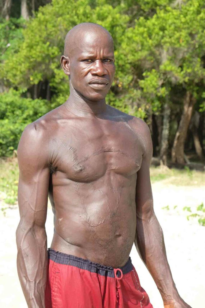 Augustino Openon steht oberkörperfrei am Strand