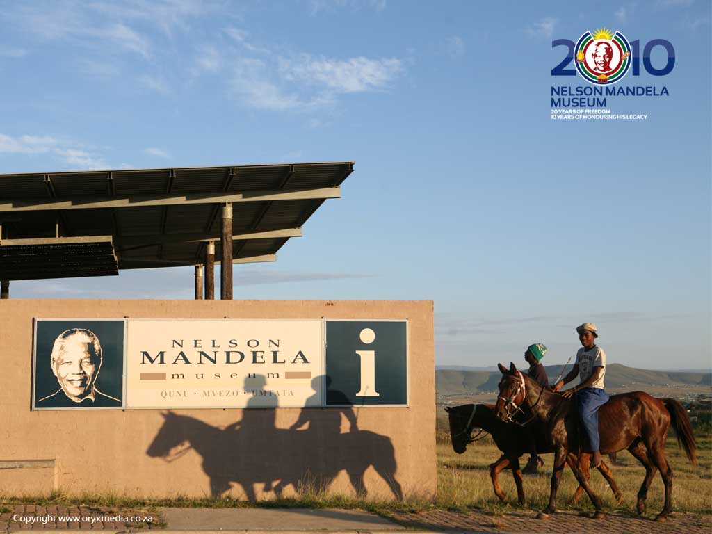 Zwei junge Männer auf Pferden neben einem Wegweiser zum Nelson Mandela Museum